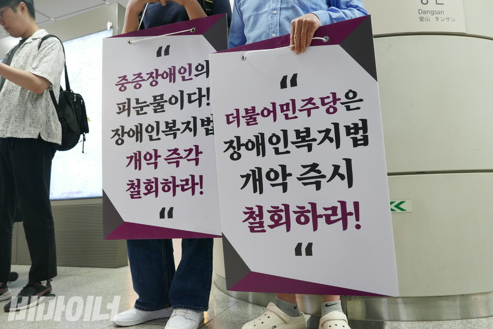 활동가 두 명이 전장연 지하철 선전전에서 “중증장애인의 피눈물이다! 장애인복지법 개악 즉각 철회하라! 더불어민주당은 장애인복지법 개악 즉시 철회하라!”라고 적힌 피켓을 들고 있다. 사진 양유진