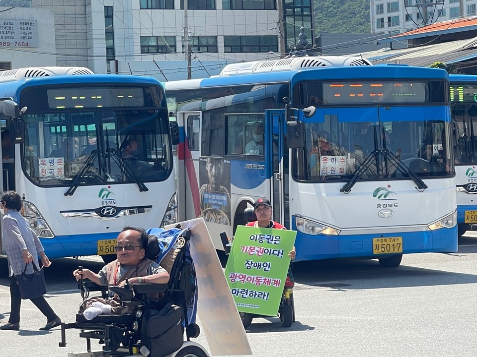 휠체어 이용 활동가들이 계단버스 앞에 있다. 문경희 세종장차연 대표는 “이동권은 기본권이다! 장애인 광역이동체계 마련하라!”라는 피켓을 목에 걸었다. 사진 전장연