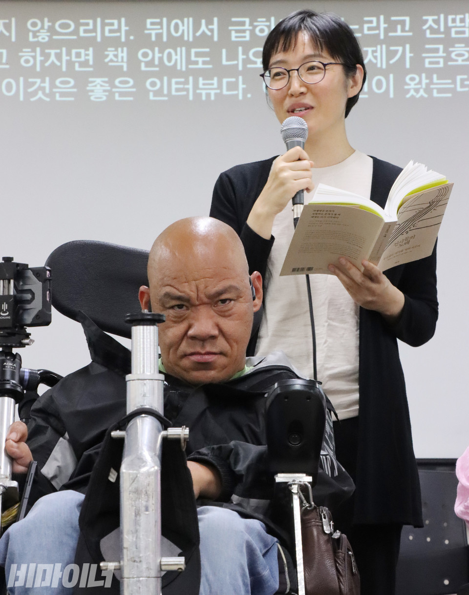 홍은전 작가가 이규식 서울장애인차별철폐연대 대표 이야기를 낭독하고 있다. 바로 앞에서 이규식 대표가 심각한 표정을 짓고 있다. 사진 이슬하
