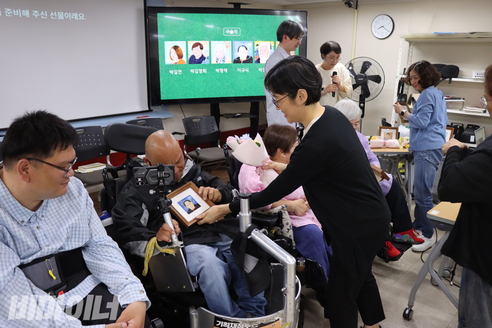 액자에 표구한 훗한나 작가의 일러스트를 꽃과 함께 구술자들에게 선물하고 있다. 사진 이슬하