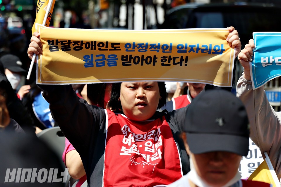 박경인 활동가가 지난 5월 1일 열린 두 번째 장애인 노동절 결의대회에서 “발달장애인도 안정적인 일자리와 월급을 받아야 한다”라고 적힌 작은 현수막을 펼쳐 보이고 있다. 사진 하민지
