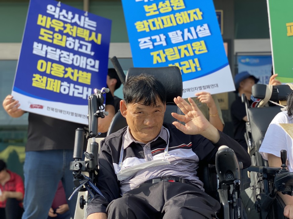 김홍기 노들장애인야학 활동가 뒤로 “익산시는 바우처택시 도입하고 발달장애인 이용차별 철폐하라”, “보성원 학대피해자 즉각 탈시설 자립지원하라”라고 적힌 피켓이 보인다. 사진 전북장차연