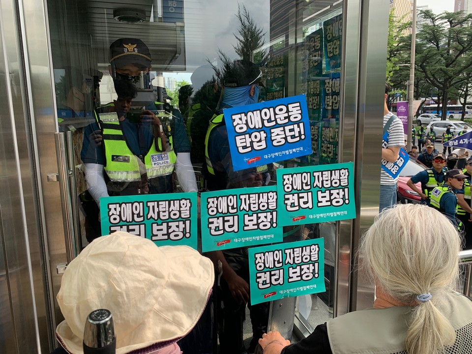 장애인 활동가들이 “장애인운동 탄압 중단”, “장애인자립생활 권리 보장” 등의 문구가 적힌 스티커를 대구시당 정문 앞에 붙였다. 경찰들이 정문에 누구도 출입할 수 없도록 막고 있다. 사진 대구장차연
