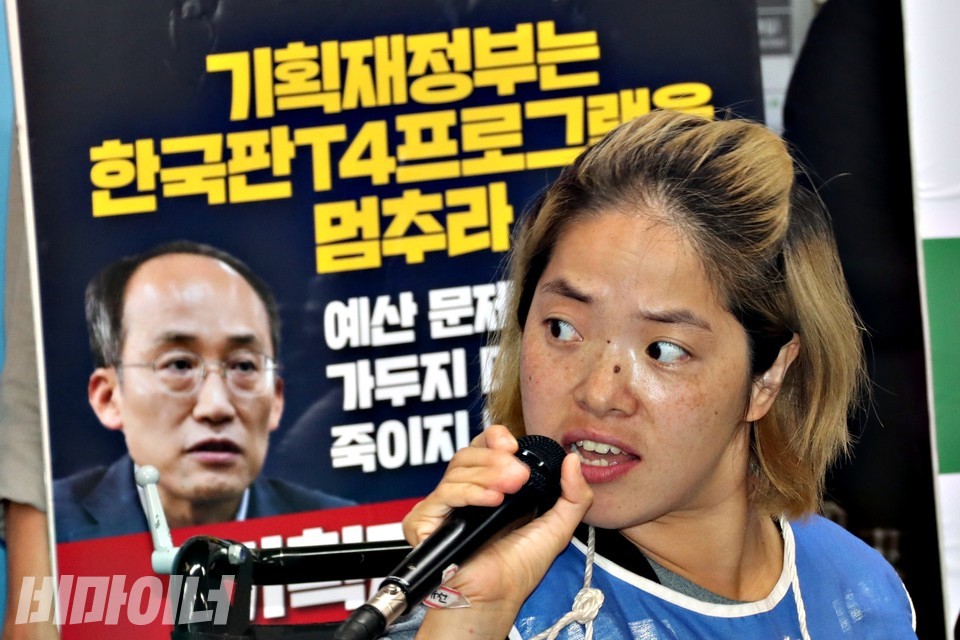 문애린 이음장애인자립생활센터 소장이 발언 중이다. 그의 뒤에 추경호 기획재정부 장관의 사진이 담긴 피켓이 있다. 피켓에는 “기획재정부는 한국판T4프로그램을 멈추라”라고 적혀 있다. 사진 하민지
