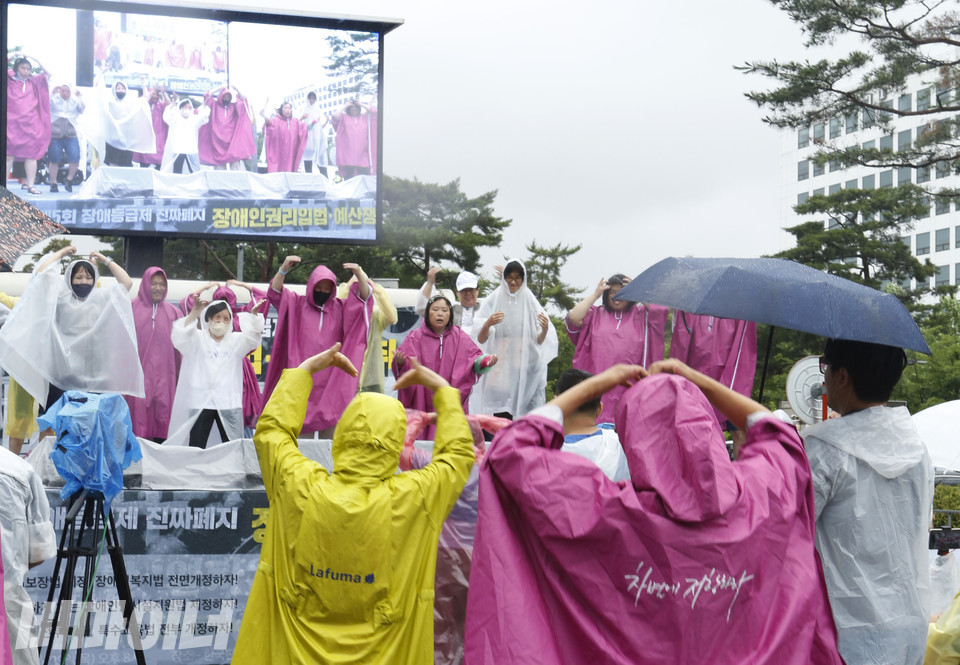 김포장애인야학 권리중심공공일자리 캠페이너 노동자들이 폭우 속에서 노래에 맞춰 춤을 추며 문화예술 직무를 수행하고 있다. 사진 박소연