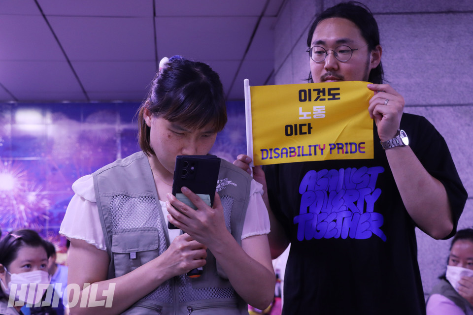 경기도 권리중심공공일자리 노동자 엄소현 씨가 발언하고 있다. 그 옆에서 우정규 활동가가 “이것도 노동이다”라고 적힌 깃발을 펼쳐 보인다. 사진 강혜민