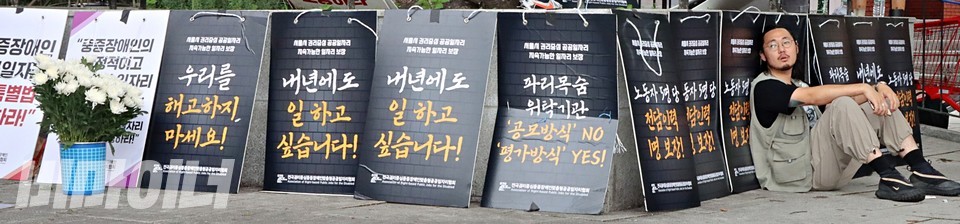 우정규 전권협 활동가가 앉아 있다. 그의 뒤로 “우리를 해고하지 마세요”, “내년에도 일하고 싶습니다”라고 적힌 피켓들이 늘어져 있다. 제일 왼쪽에는 국화꽃이 있다. 사진 하민지