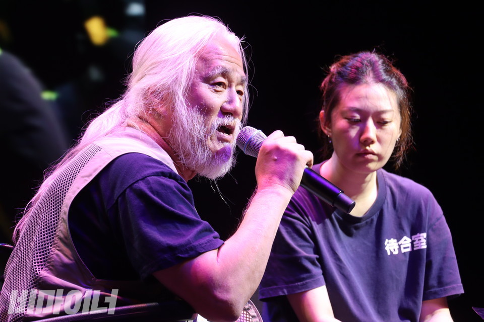 노들노래공장 수업을 하는 만수(가수 이민휘) 교사와 어깨꿈(박경석 전국장애인차별철폐연대 대표)이 ‘T4’ 노래를 부르고 있다. 그 뒤로 지하철 투쟁 영상이 펼쳐지고 있다. 사진 강혜민