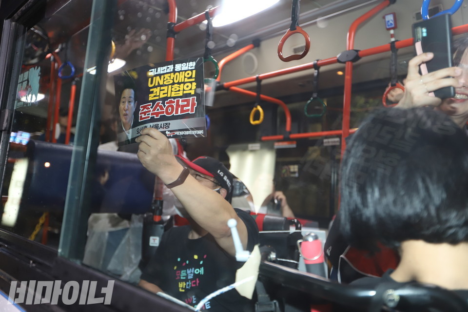 버스 안에서 장애인 활동가가 “국내법과 동일한 유엔장애인권리협약 준수하라”고 적힌 피켓을 바깥을 향해 들어 보이고 있다. 사진 강혜민