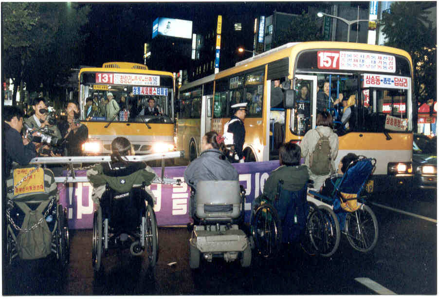 2001년 10월 31일, 종로에서 장애인들이 사다리를 목에 걸고 쇠사슬로 서로를 묶은 채 장애인은 탈 수 없는 버스를 막아서고 있다. 이 투쟁은 교통약자이동편의증진법 제정으로 이어졌다. 사진 제공 장애인이동권연대