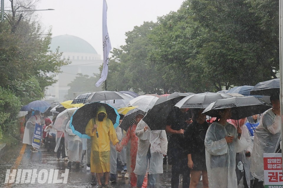 전장연 활동가들이 뇌우 속에서 국회의사당을 등지고 행진하고 있다. 사진 하민지