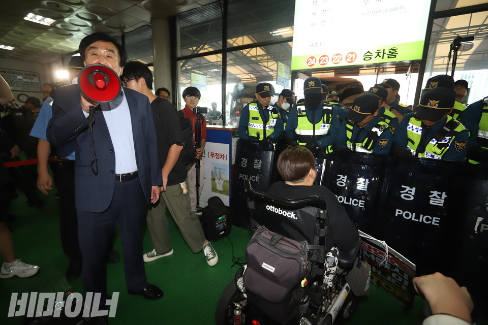 장애인 활동가들이 돈을 주고 산 버스표를 들고 승차홈에 들어서려고 하자 경찰이 가로막았다. 그 옆에서 동서울터미널 측 관리자가 확성기를 이용해 “동서울터미널은 전동휠체어 탑승 수송의 의무가 없다”고 말하고 있다. 사진 강혜민