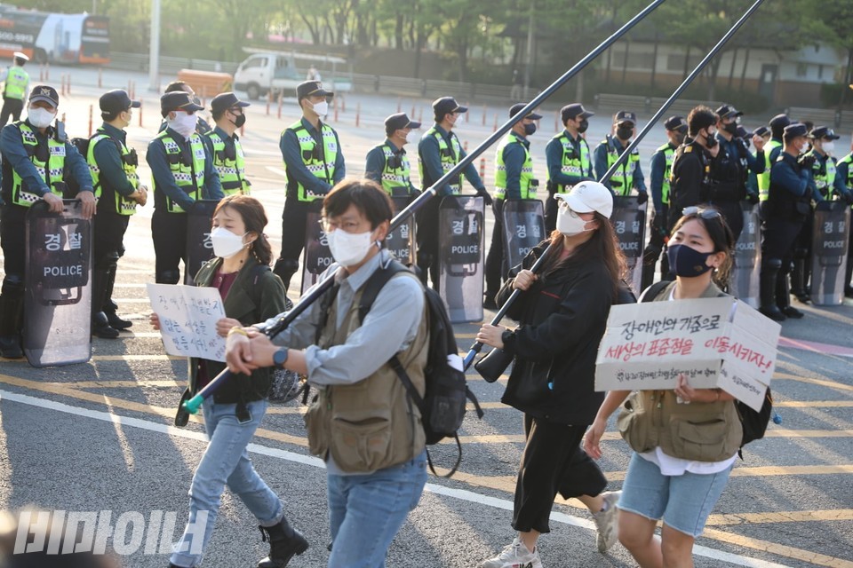 깃발과 피켓을 들고 행진하는 사람들. 그 뒤로 방패를 들고 무장한 경찰들이 보인다. 사진 강혜민 
