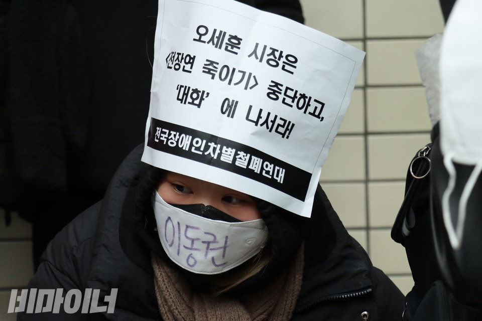 한 활동가가 이마에 “오세훈 시장은 전장연 죽이기 중단하고 대화에 나서라”라고 적힌 피켓을 붙였다. 이동권이라고 적힌 마스크도 썼다. 사진 하민지