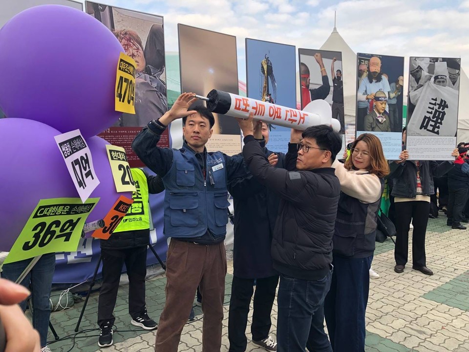보라색 풍선에 쟁의행위로 인해 생겨난 손해배상금 수십 억이 적힌 종이가 붙어 있다. 사람들이 ‘노란봉투법’이라 적힌 커다란 바늘로 풍선을 터뜨리려 하고 있다. 사진 노조법 2·3조 개정 운동본부