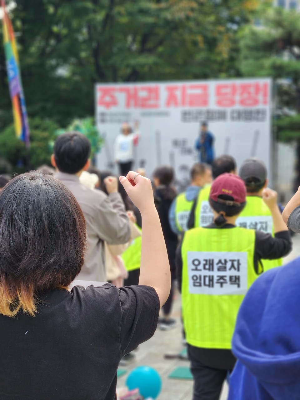 지난 10월 14일 진행된 빈곤철폐 대행진 집회 현장. 집회 무대에 “주거권 지금 당장”이라 적혀 있다. 한 집회 참가자의 등에는 “오래 살자 임대주택”이라는 문구가 적혀 있다. 사진 개신교참가단