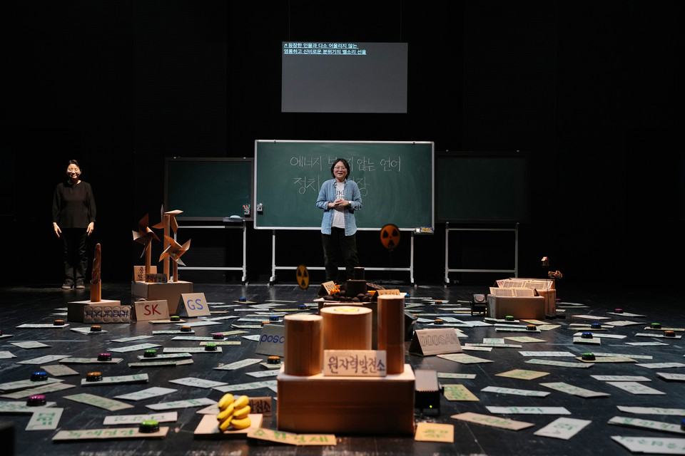 수어통역사가 함께한 〈에너지_보이지 않는 언어〉 무대: 칠판 앞에 등장인물 지연이 서 있고, 칠판 위에는 문자통역 화면이 있다. 관객 시점에서 무대 왼편에 검은 옷을 입은 수어통역사가 자리하고 있다 ©옥상훈·2023 SPAF
