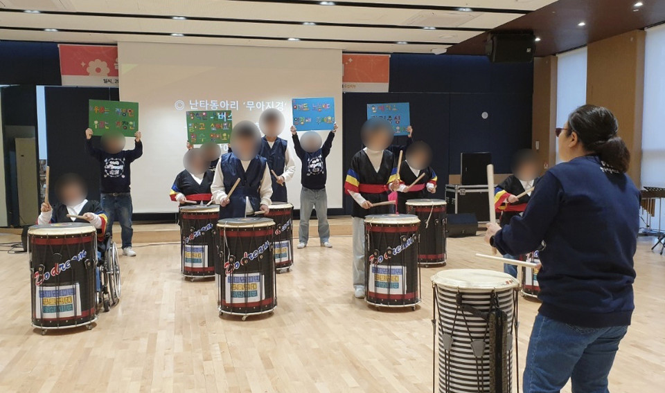 경기장애인부모연대 오산지회는 2023년 12월 7일 권리중심공공일자리 사업 보고를 위한 음악회를 열었다. 난타동아리 ‘무아지경’이 공연을 하고 있고 그 뒤에서 권리중심공공일자리 노동자들이 “일하고 싶어요. 할 수 있어요.” “이것도 노동이다. 인정해 주세요.” “함께해요 권리중심공공일자리” 등 권리중심공공일자리를 알리는 피켓을 들고 있다. 사진 제공 유경애