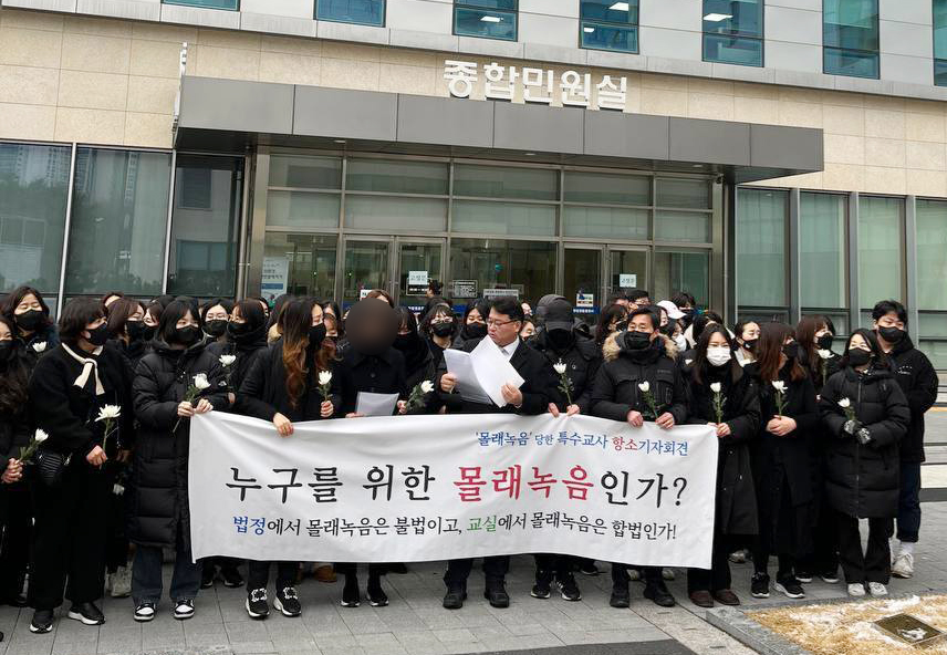 웹툰 작가 주호민 씨의 자녀를 정서적으로 학대한 혐의로 1심에서 유죄 선고를 받은 특수교사 ㄱ씨가 6일 오전 항소장을 제출하면서 수원지법 앞에서 기자회견을 열었다. 현수막에는 “‘몰래 녹음’ 당한 특수교사 항소 기자회견. 누구를 위한 몰래 녹음인가? 법정에서 몰래 녹음은 불법이고, 교실에서 몰래 녹음은 합법인가”라고 적혀 있다. 동료 교사들이 검은 옷에 하얀 국화를 들고 있다. 사진 경기교사노동조합