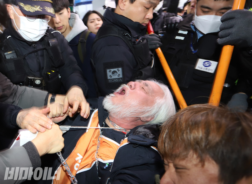 박경석 전장연 대표가 끌려 나가지 않기 위해 쇠사슬을 그의 옆에 있는 장애인 활동가의 전동휠체어와 묶었다. 서울교통공사와 경찰이 쇠사슬을 자르는 과정에서 무리하게 진압하면서 그의 목이 쇠사슬과 우드락피켓의 끈에 의해 졸리고 있다. 순간 숨통이 막히면서 박 대표의 얼굴이 시뻘겋게 달아올랐다. 사진 강혜민