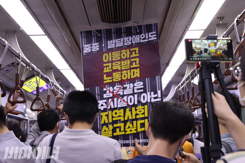 지하철 안에서 한 활동가가 “중증·발달장애인도 이동하고 교육받고 노동하며 감옥 같은 거주시설이 아닌 지역사회 살고 싶다”라고 적힌 피켓을 높이 들고 있다. 사진 강혜민