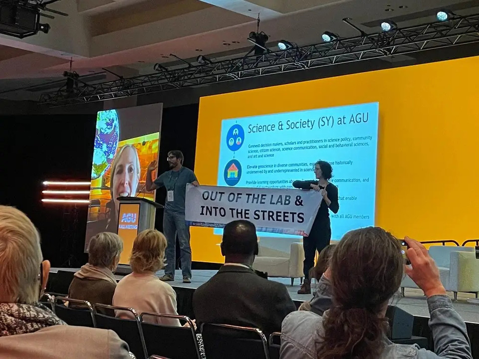 2022년 12월 15일, AGU 2022 정기 가을학술대회가 열리던 중 피터 칼무스와 로즈 아브라모프가 무대에 올라 ‘행동하자’라는 구호를 외치고 있다. 사진 Rose Abramoff