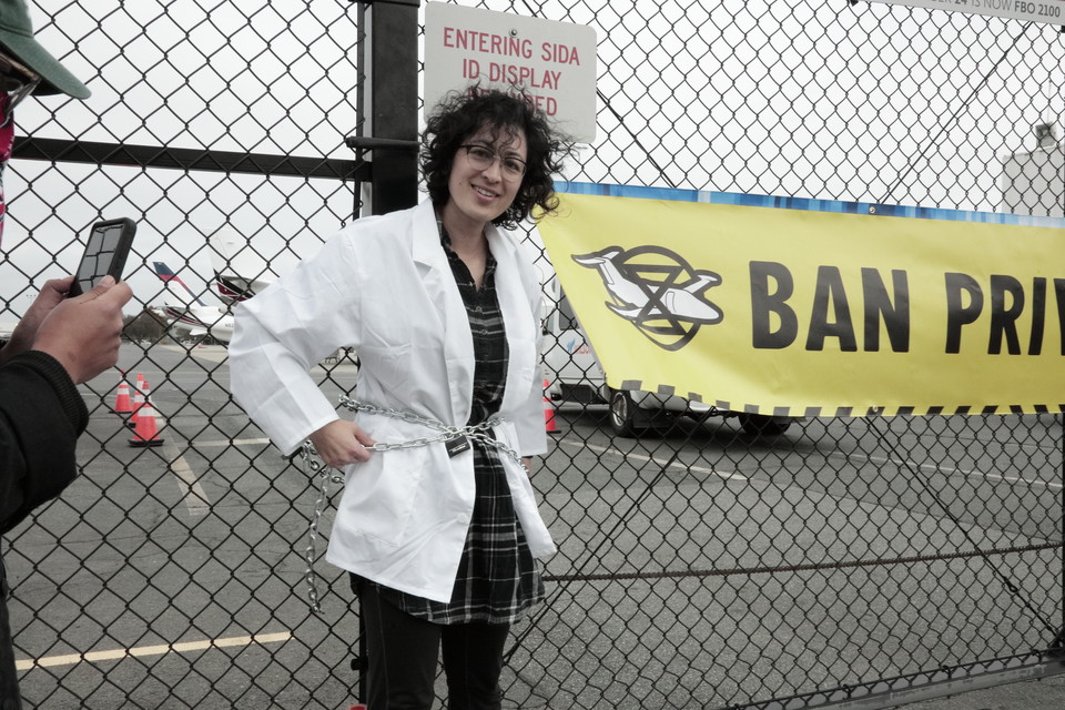 2022년 11월 샬럿 더글러스 공항 전용기 터미널에서 쇠사슬로 몸을 묶고 통로를 막은 로즈. 그의 오른편 현수막에는 ‘개인 전용기 폐지(BAN PRIVATE JETS)’라는 문구가 적혀 있다. 사진 William Dickson(@stills.will)