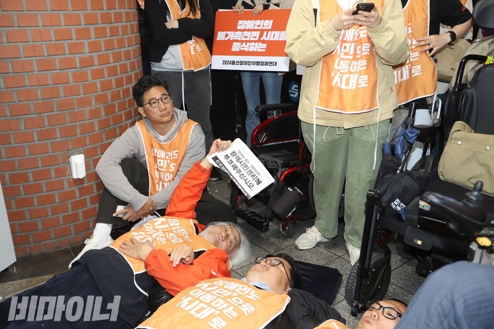 바닥에 누운 박경석 대표가 “장애시민권리에 투표해 주십시오”라는 문구가 적힌 종이를 들어 보이고 있다. 사진 강혜민