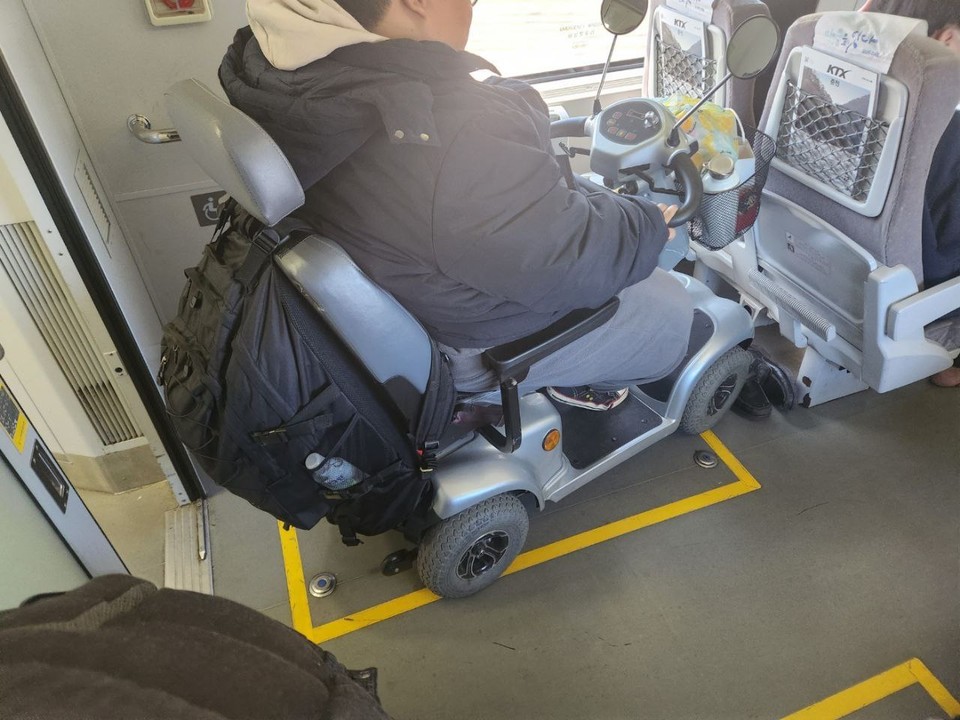 2023년 11월, 노지성 씨가 KTX-산천 열차 전동휠체어 좌석이 협소하여 전동스쿠터를 똑바로 세우지 못한 채 탑승한 모습. 휠체어석은 출입구 바로 앞에 붙어있다. 사진 장애인차별금지추진연대 제공