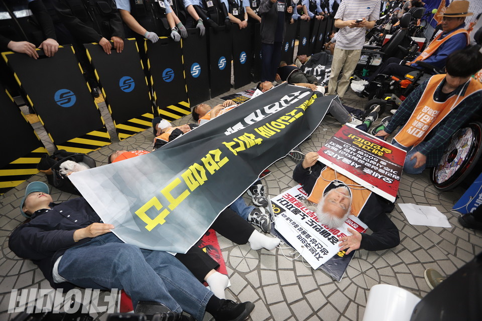 14일 오전, 전장연이 제3차 출근길 지하철 승강장 ‘다이인(die-in) 행동’을 진행하고 있다. 참여자들은 “시민 여러분, 장애인도 시민으로 살고 싶습니다”라고 적혀있는 플랜카드를 덮고 누워있다. 사진 김소영