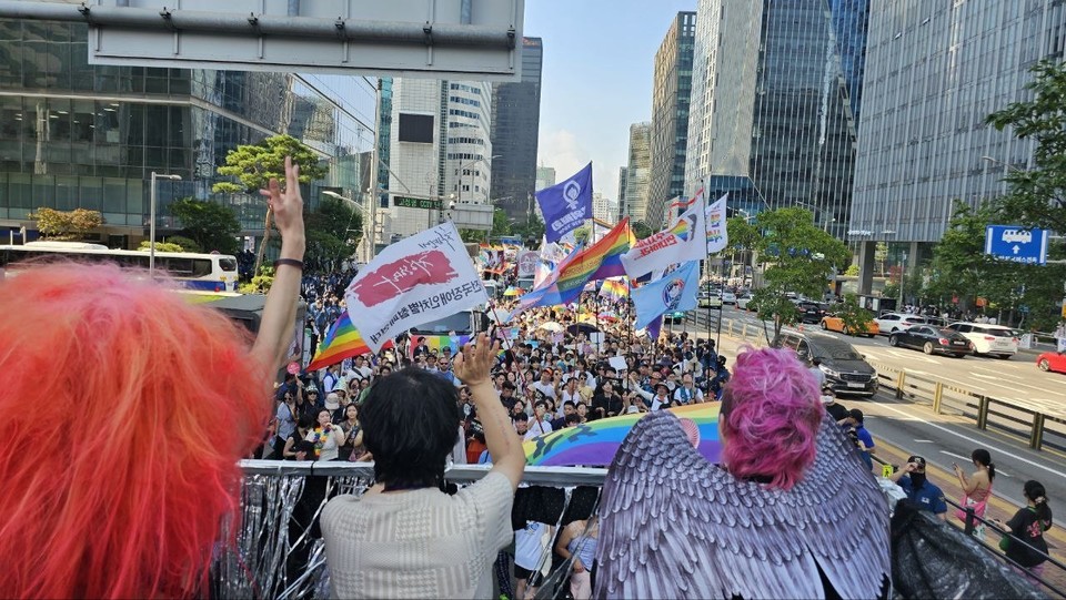 2023년 서울퀴어문화축제 ‘퀴어한 몸들의 수상한 연대 행진’ 현장. 트럭을 따라 오는 긴 행렬을 향해 트럭 위의 세 사람이 손을 흔들고 있다. 사진 지오