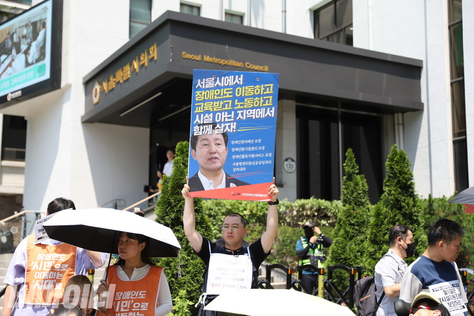 기자회견 참가자가 “서울시에서 장애인도 이동하고 교육받고 노동하고 시설 아닌 지역에서 함께 살자!”라고 쓰인 피켓을 높이 들고 있다. 사진 김소영