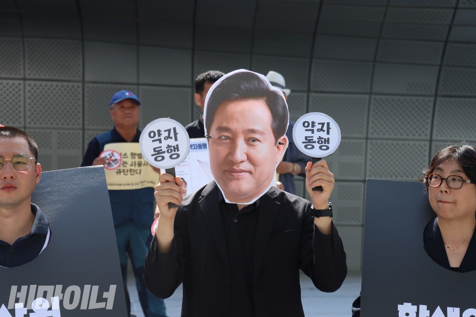 웃고 있는 오세훈 서울시장 가면을 쓴 활동가가 “약자 동행”이라고 쓰인 피켓을 양손에 들고 있다. 사진 김소영