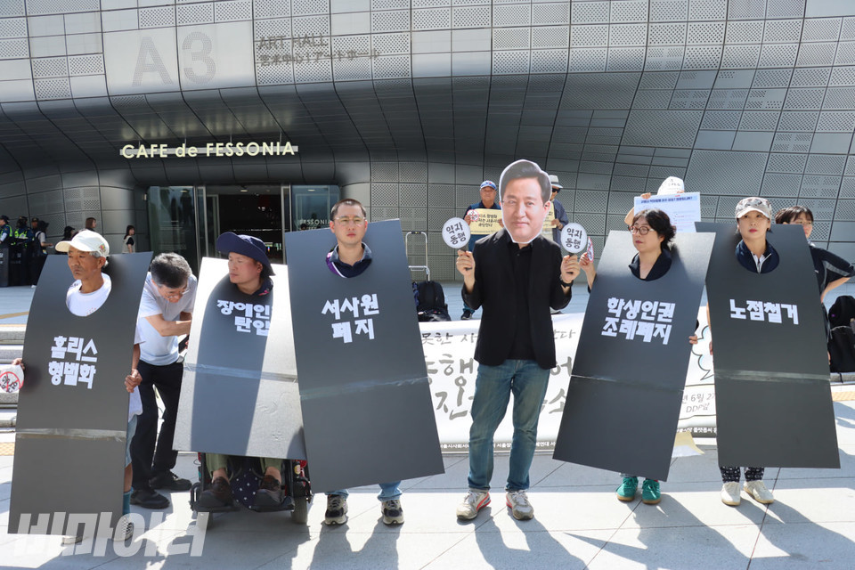 기자회견 참가자들이 퍼포먼스를 진행하고 있다. 오세훈 서울시장 가면을 쓴 활동가 주변으로 퍼포먼스 참가자들이 “홈리스 형벌화”, “장애인권 탄압”, “서사원 폐지”, “학생인권조례 폐지”, “노점 철거”라고 쓰인 피켓을 목에 걸고 있다. 사진 김소영