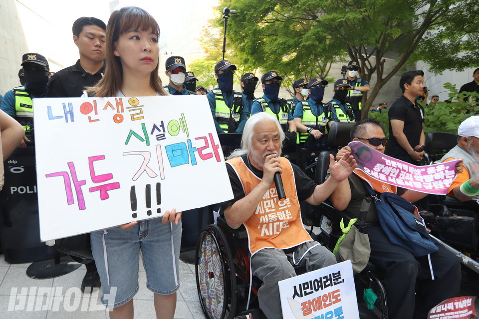 박경석 전장연 상임공동대표가 발언하고 있다. 그 옆에서 피플퍼스트 발달장애인 활동가가 “내 인생을 시설에 가두지 마라”고 적힌 피켓을 들고 있다. 사진 강혜민