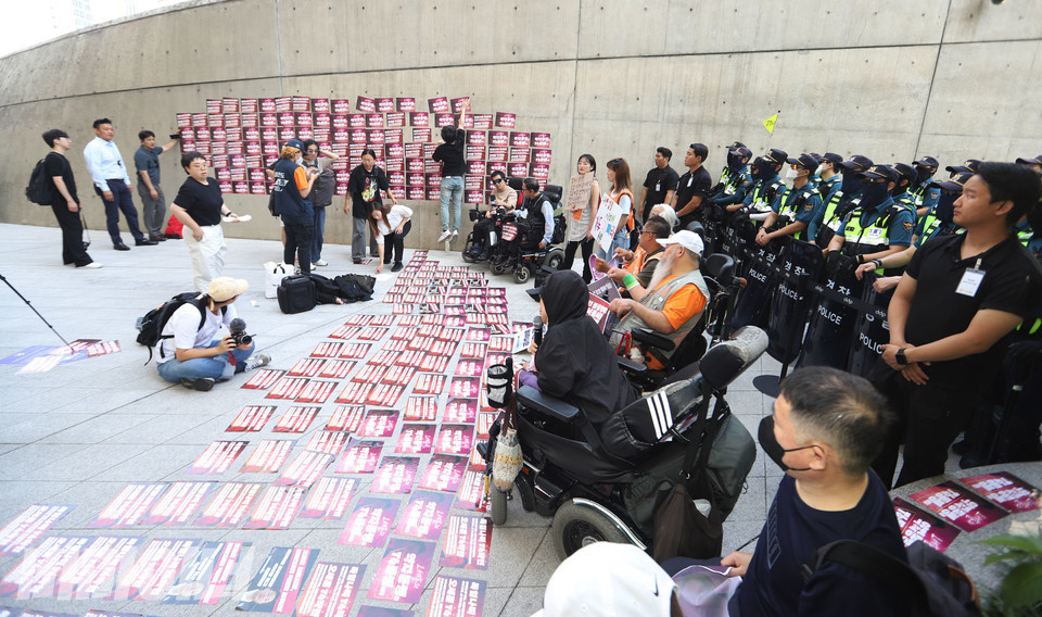 전장연이 서울시의 ‘서울약자동행포럼’이 열리는 DDP 앞에서 이를 비판하며 ‘오세훈 서울시장 장애인 권리 약탈 포럼’을 열고 있다. 바닥과 벽면에 이를 규탄하는 붉은색 스티커가 붙어 있다. 사진 강혜민