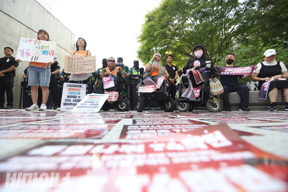27일, 서울장차연이 서울시의 ‘서울약자동행포럼’이 열리는 DDP 앞에서 이를 비판하며 ‘오세훈 서울시장 장애인 권리 약탈 포럼’을 열고 있다. 바닥에는 이를 규탄하는 붉은색 스티커가 붙어 있다. 사진 강혜민