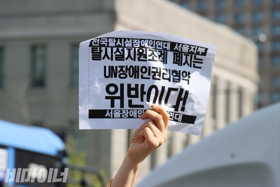 한 사람이 “탈시설지원조례 폐지는 유엔장애인권리협약 위반이다!”라고 적힌 종이를 높이 들고 있다. 사진 김소영