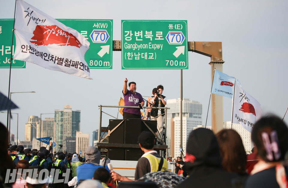 사람들이 마포대교를 건너고 있다. 박철균 전장연 활동가가 트럭 위에서 선동 발언을 하고 있다. 사진 최인기