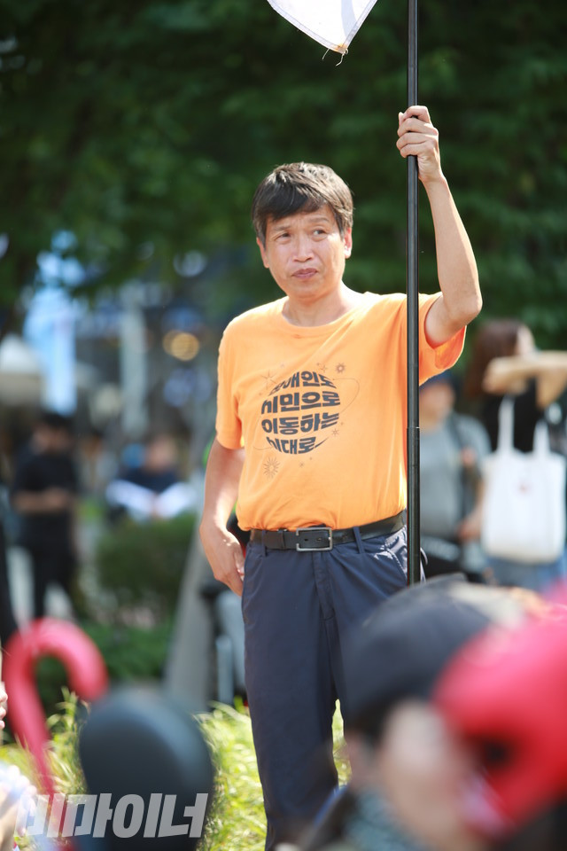 한 활동가가 ‘장애인도 시민으로 이동하는 시대로’라고 적힌 단체 티셔츠를 입고 깃발을 들고 있다. 사진 최인기