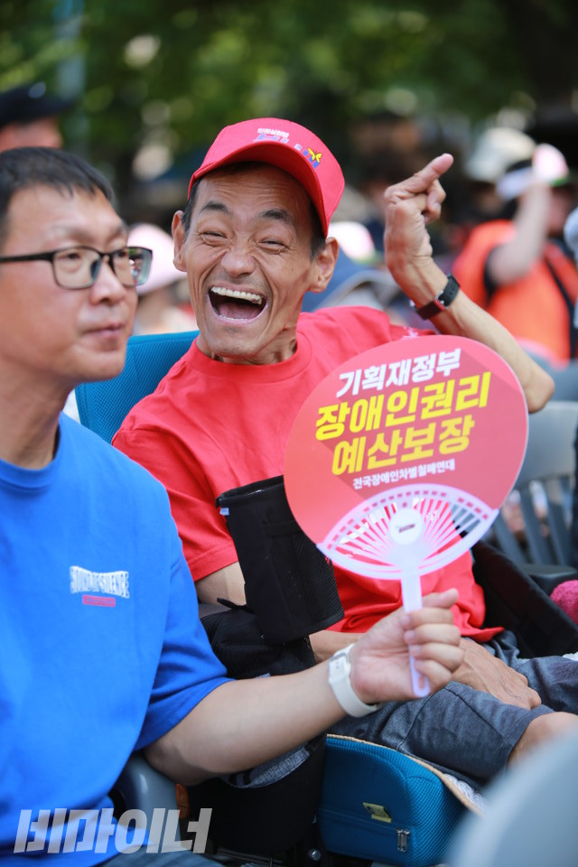 전동행진에 참여한 장애인 활동가가 활짝 웃어 보이고 있다. ‘기획재정부 장애인권리 예산 보장’이라고 적힌 부채가 보인다. 사진 최인기