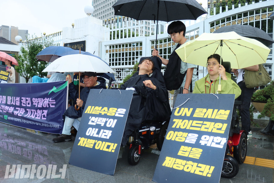 18일 오전 11시, 쏟아지는 폭우 속 서울장차연은 정부서울청사 본관 앞에서 권익위 규탄 기자회견을 열었다. 참여자들이 “시설수용은 ‘선택’이 아니라 ‘차별’이다!“, “UN탈시설가이드라인 이행을 위한 법을 제정하라!”라고 적힌 피켓을 자신의 휠체어 앞에 세워뒀다. 사진 김소영