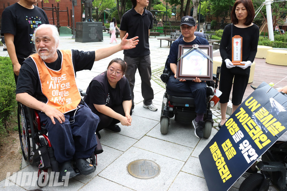 2009년 6월, 62일간 농성했던 마로니에공원에는 이를 기념하는 동판이 바닥에 새겨져 있다. 박경석 전장연 상임공동대표가 유족들에게 당시 상황에 대해 설명하고 있다. ‘마로니에 8인’으로 고인과 함께 농성했던 김동림 김포장애인야학 교감이 영정을 들고 있다. 사진 강혜민