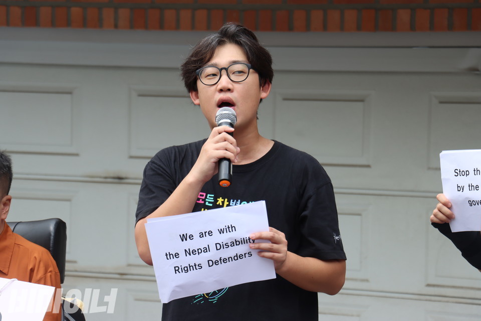 재민 전국장애인차별철폐연대 활동가가 발언하고 있다. 그의 손에는  “We are with the Nepal Disability Rights Defenders”(우리는 네팔 장애인권리 옹호자들과 함께한다)라고 적힌 피켓이 들려 있다. 사진 김소영