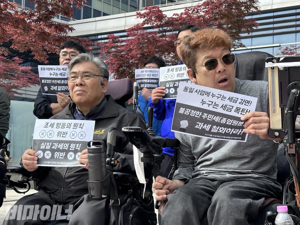 4월 26일, 서울행정법원 앞에서 열린 기자회견에서 장애인 활동가들이 무거운 표정으로 ‘조세평등의 원칙 위반, 실질 과세의 위반’이라고 적힌 손피켓을 들고 있다. 사진 강혜민