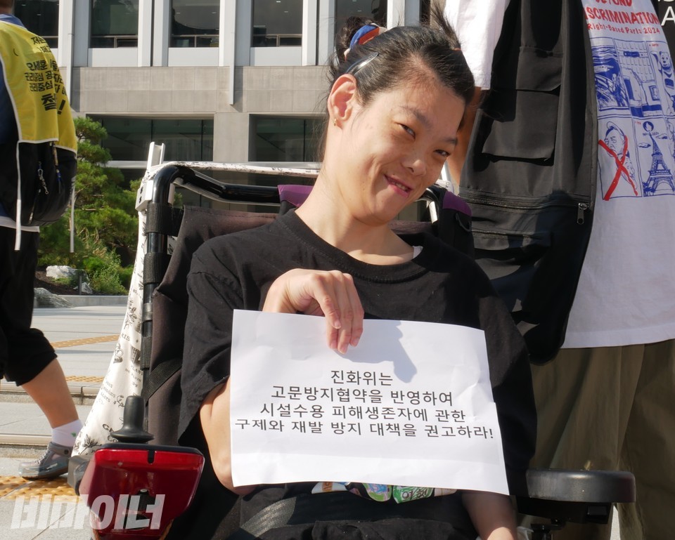 최영은 활동가가 “진화위는 고문방지협약을 반영하여 시설수용 피해생존자에 관한 구제와 재발 방지 대책을 권고하라!”라고 적힌 피켓을 들고 있다. 사진 하민지