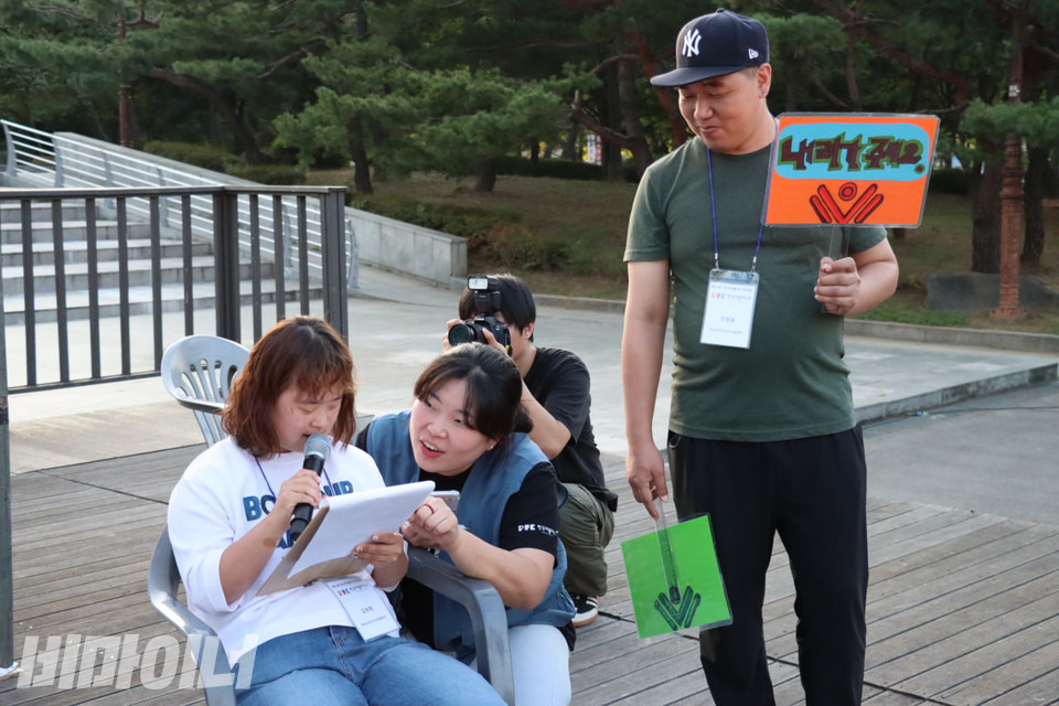 김보희 함세상장애인자립생활센터 활동가가 의자에 앉아 자유발언 사회를 보고 있다. 옆에 있는 활동가는 발언이 3분이 지나면 발언을 제지하기 위해 ‘내려가주세요’라고 적힌 팻말을 들고 있다. 사진 김소영