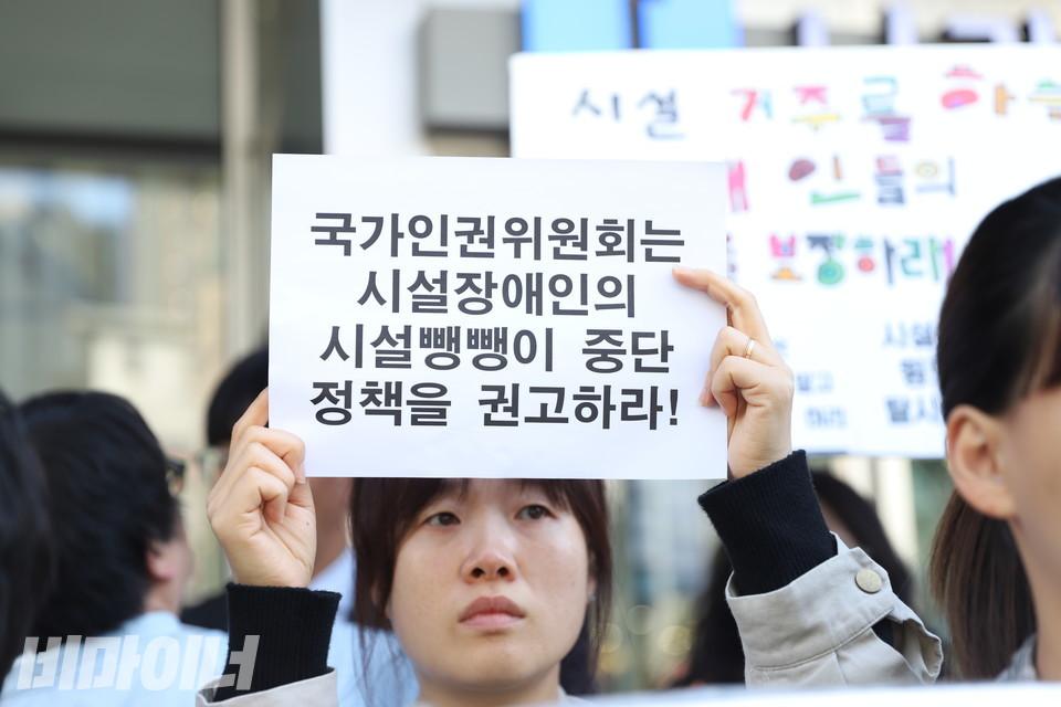 기자회견 참가자가 “국가인권위원회는 시설장애인의 시설뺑뺑이 중단 정책을 권고하라!”라고 적힌 종이 피켓을 들고 있다. 사진 김소영