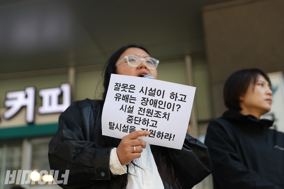 기자회견 사회를 맡은 민푸름 서울장차연 활동가가 종이 피켓을 들고 발언하고 있다. 피켓에는 “잘못은 시설이 하고 유배는 장애인이? 시설 전원조치 중단하고 탈시설을 지원하라!”고 적혀있다. 사진 김소영
