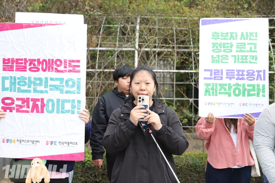  이다영 피플퍼스트광진센터 활동가가 발언하고 있다. 이 활동가의 왼쪽에는 “발달장애인도 대한민국의 유권자이다!”라고 적힌 피켓이, 오른쪽에는 “후보자 사진, 정당 로고, 넓은 기표칸 그림 투표용지 제작하라!”라고 적힌 피켓이 보인다. 사진 김소영